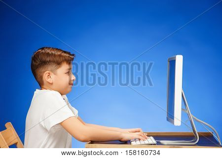School-age boy sitting in front of the monitor laptop at blue studio backgroubd