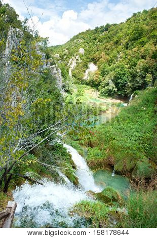 A river meandering between stone hills of the canyon. Waterfall falling down into a pond. Sunny day white fluffy clouds in the sky. Plitvice lakes national park Croatia