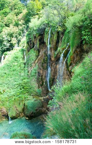 High waterfall among green foliage. Water falling from brown rocks into a clear turquoise pond. Plitvice lakes national park Croatia