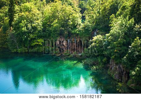 Lake with transparent emerald water. Waterfall among red rocks and foliage. Plitvice lakes national park Croatia