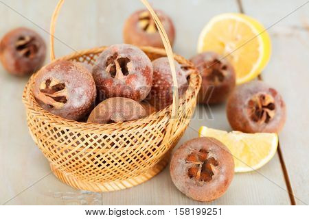 Ripe common medlar fruit in the basket. Medlars and Lemon slices on blue wooden board.
