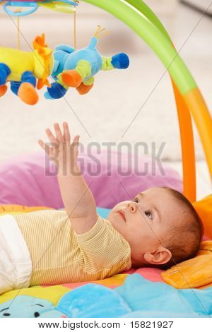 เด็กเอื้อมคว้าของเล่นที่มีสีสันบน playmat