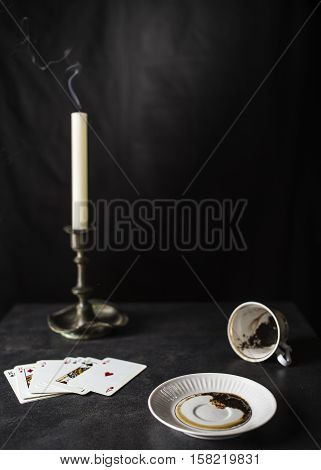 Fortune teller reading coffee grounds in the state are near a deck of cards and a candle in the old candlestick against the black background
