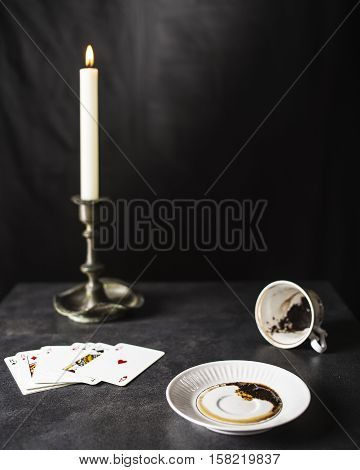 Fortune teller reading coffee grounds in the state are near a deck of cards and a candle in the old candlestick against the black background