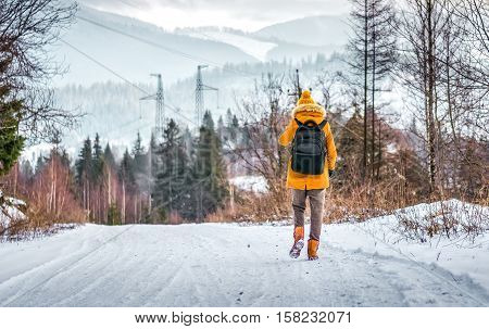 woman traveler walking along the winter mountain road in the woods