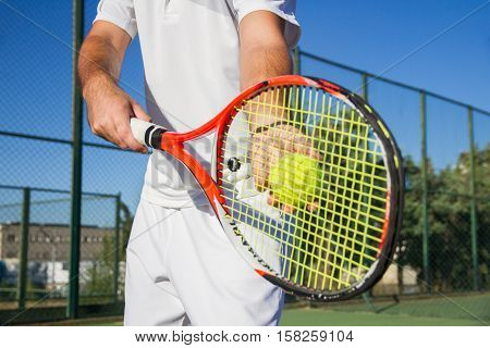 Close up photo of a racket and a tennis ball. Both are held by a professional tennis player with his hands while dispute a match against another player.