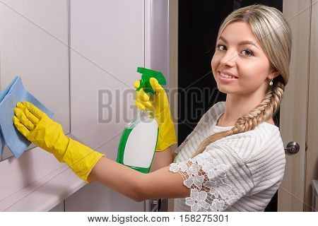 Young smiling lady wiping mirror with the help of blue cloth and special cleaning products
