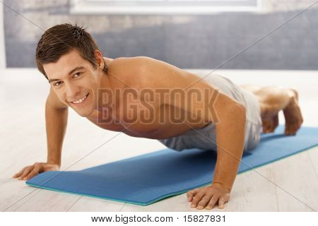 Goodlooking Mann doing Push up in Turnhalle, Training auf Schaumstoff-Matratze, lächelnd in die Kamera.?