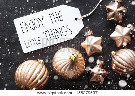 Label With English Quote Enjoy The Little Things. Bronze Christmas Tree Balls On Black Paper Background With Snowflakes. Christmas Decoration Or Texture. Flat Lay View