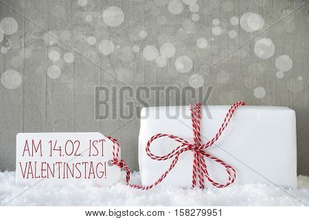 One Christmas Gift Or Present On Snow. Cement Wall As Background With Bokeh. Modern And Urban Style. Card For Birthday Or Seasons Greetings. Label With German Text Valentinstag Means Valentines Day