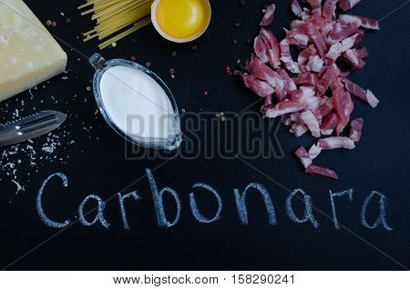 Ingredients for Pasta Carbonara on dark background with word Carbonara. Set of products for pasta Carbonara - spaghetti bacon cream Parmesan cheese egg. Italian food concept. Top view.