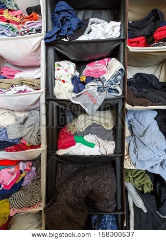 Messy untidy wardrobe closeup with colorful clothes for men women baby