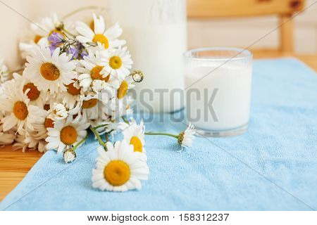 Simply stylish wooden kitchen with bottle of milk and glass on table, summer flowers camomile, healthy foog moring concept noone close up