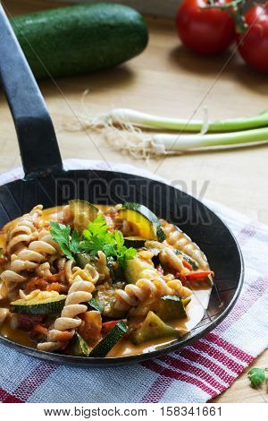black iron pan with wholewheat pasta and zucchini tomato vegetables on a kitchen towel and a wooden worktop healthy vegetarian diet meal vertical selected focus narrow depth of field