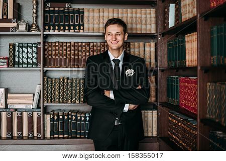Groom in a suit holding buttonhole in the library