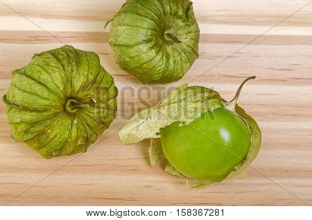 Three Whole Green Husk Tomatoes, one with loose husk on table