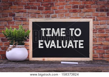 TIME TO EVALUATE word on blackboard with green plant
