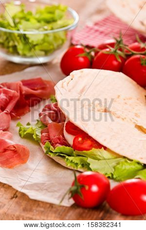 Piadina with ham and lettuce on wooden table.