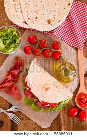 Piadina with ham and lettuce on wooden table.
