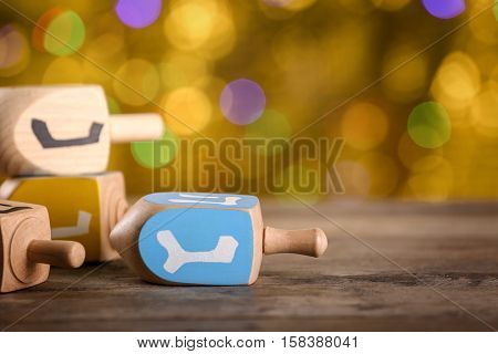 Dreidels for Hanukkah on wooden table against defocused lights, close up