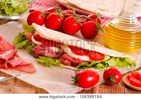 Piadina with ham and lettuce on wooden table.