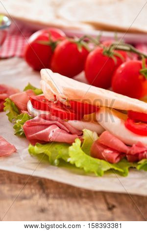 Piadina with ham and lettuce on wooden table.