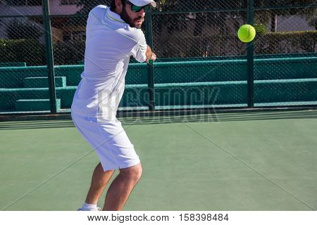 Professional tennis player playing a game of tennis on a court. He is about to hit the ball with the racket. The ball is suspended in the air.