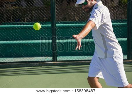 Professional tennis player playing a game of tennis on a court. He is about to hit the ball with the racket. The ball is suspended in the air.