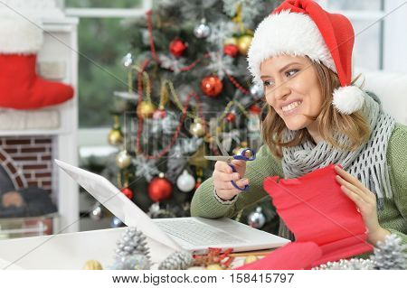 Portrait of young smiling woman in Santa hat preparing for Christmas, making hand made decoration
