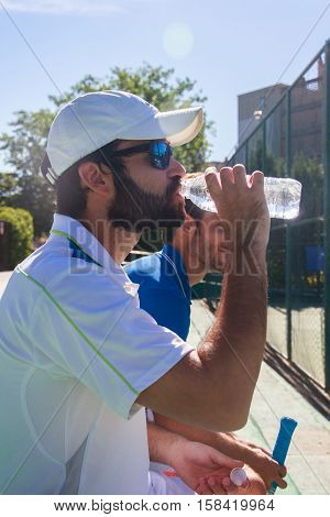 Two professional players hydrating after a hard game of tennis. They are friends and are sitting resting for the game. They are happy and laughing.