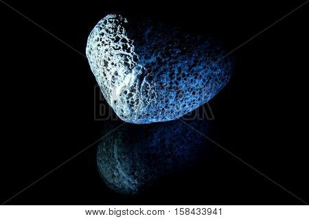 Stone similar to the moon lies on the reflecting surface. The background is black.