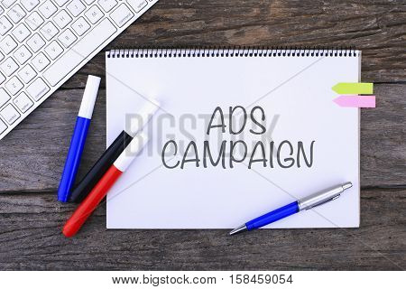 Notebook with ADS CAMPAIGN Handwritten on wooden background and Modern Computer Keyboard. Top View Composition