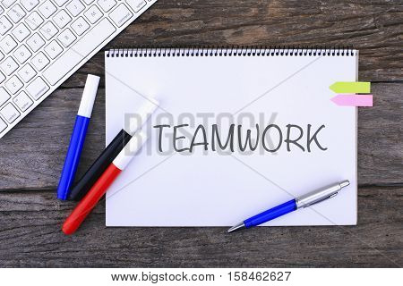 Notebook with TEAMWORK Handwritten on wooden background and Modern Computer Keyboard. Top View Composition
