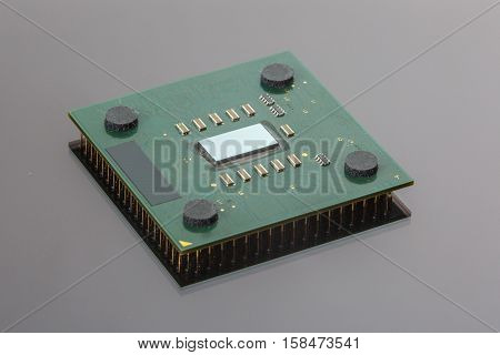 CPU. Modern computer processor unit. The microprocessor is located on a green PCB. 4 mounting pads on the card and microelements around the processor chip. Isolated on gray. Pins reflection.