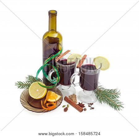 Mulled wine in two glass mugs with slices of lemon bottle of red wine mulling spices for cooking of mulled wine and two fir branches on a light background