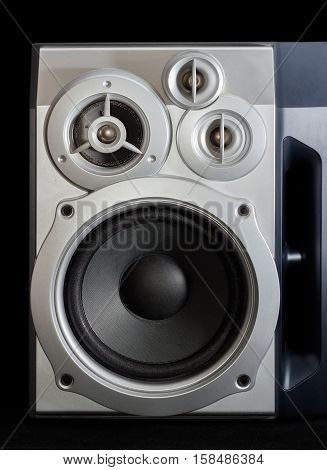 Fragment of home high fidelity three-way loudspeaker system with bass reflex port in silvery housing on a dark background