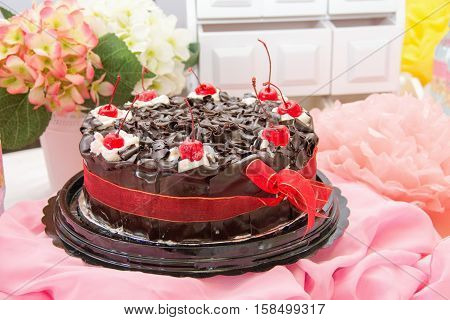 Black forest cake whole pastry decorated with whipped cream, red cherry, and dark compound flakes