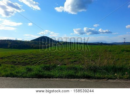 Day view on a landscape with a hill, green meadow and blue sky with a few clouds.