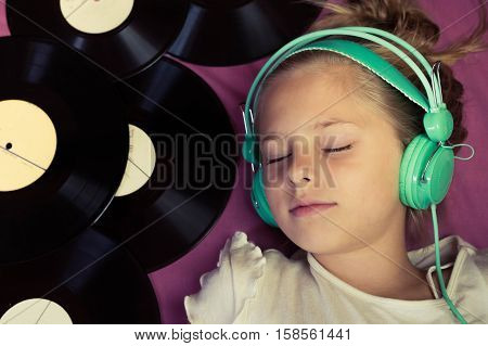 Beautiful girl lying next to vinyl records and listening to music on headphones. Top view.