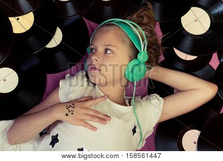 Beautiful girl lying next to vinyl records and listening to music on headphones. Top view.