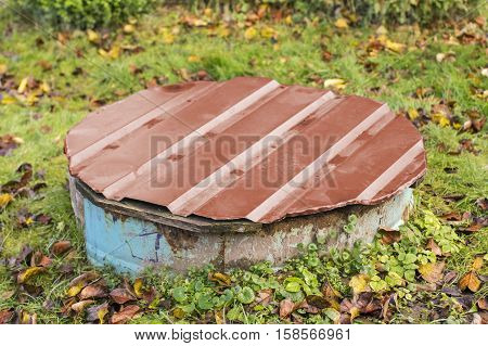 Old rustic concrete drain well with painted metallic cup in autumn