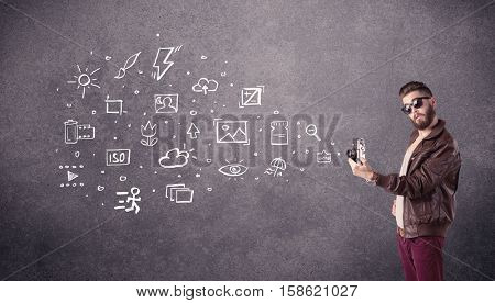 An elegant hipster guy trying to use a vintage camera with camera settings icons drawn on wall, like flash, white balace or ISO value concept