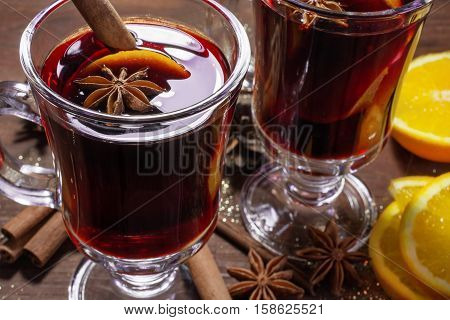 two glasses of hot mulled wine with spices and sliced orange on wooden background. close up
