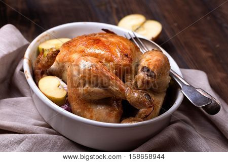 roasted chicken with apple in white ceramic pan on wooden table top view.
