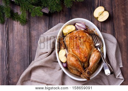 roasted chicken with apple in white ceramic pan on wooden table top view.