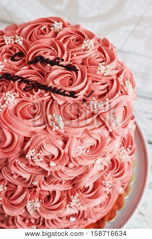 Gorgeous two-tier cake covered in roses made of butter cream icing sitting on a cake pedestal with background
