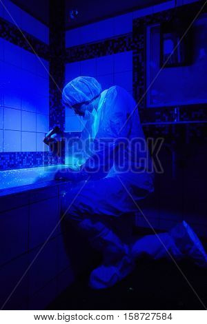 Criminologist at work under UV light in bathroom