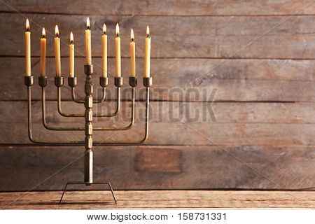Menorah with candles for Hanukkah on table against wooden background
