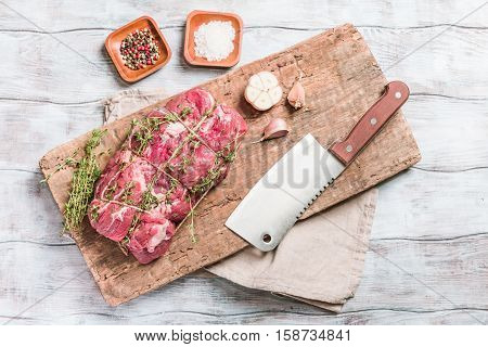 Raw roastbeef meat cut with hyme and garlic and knife on cutting board over old  wooden background, top view