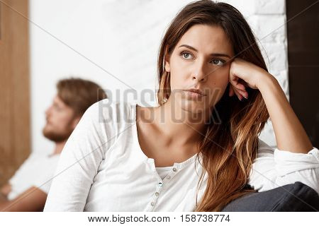 Dissapointed young beautiful brunette girl in quarrel with her boyfriend on sofa background.